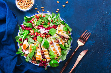 Salad with grilled chicken, spinach, arugula, cedar nuts and pomegranate seeds. Healthy food and eating concept. Top view. Blue background