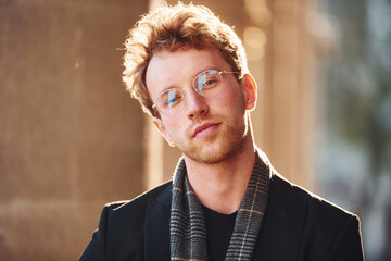 Portrait of elegant young man in glasses and formal classy clothes outdoors in the city