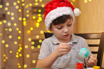 Cheerful little kid boy paints christmas balls and looks up . Holidays handmade decorations