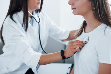 Using stethoscope. Young woman have a visit with female doctor in modern clinic