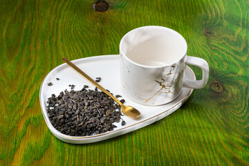 loose tea in a saucer next to a mug on a wooden background with different lighting