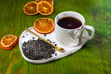 loose tea into the saucer next to the cup and sweets on the wooden background with different lighting