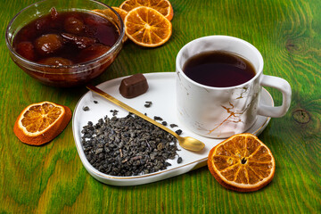 loose tea into the saucer next to the cup and sweets on the wooden background with different lighting
