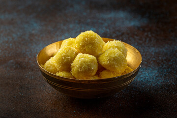 saffron flavoured desiccated coconut ladoo in a traditional metal bowl