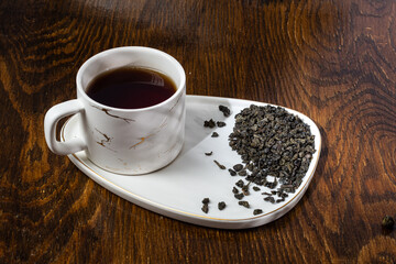 loose tea in a saucer next to a mug on a wooden background with different lighting