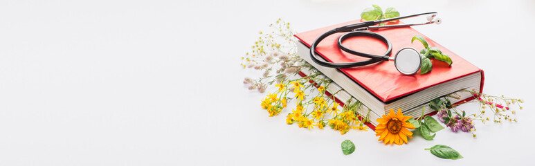 panoramic shot of herbs in book with stethoscope on white background, naturopathy concept - obrazy, fototapety, plakaty