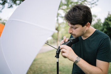 Photographer preparing outdoor photo studio while connecting umbrella diffuser. Man setting up photographer's equipment for photo shooting in nature.
