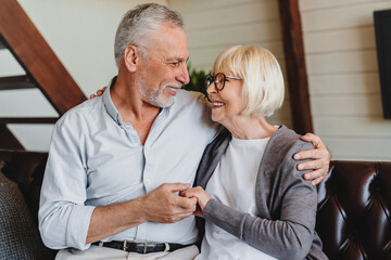 Romantic senior couple sitting close together on sofa in house smiling happilly