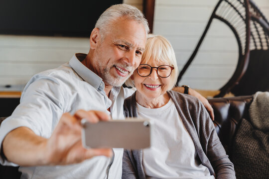 Happy Funny Senior Couple Taking Selfie Looking At Smartphone Indoor