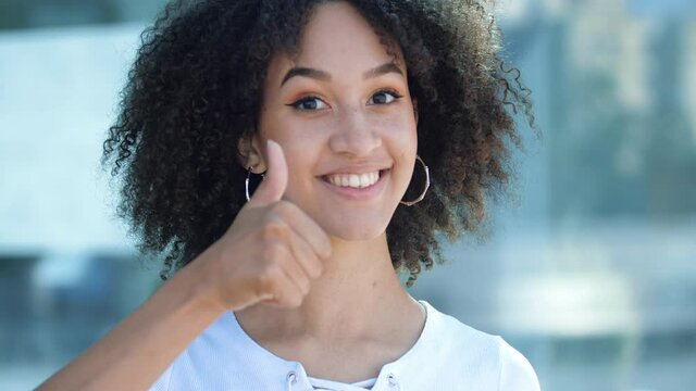 Beautiful African American positive girl with afro toothy smiles and shows thumb up, gesture of approval. Ethnic woman looks with praise, good reviews and positive feedback, success, consent and luck.