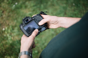Cropped man holding camera and checking photos. Close-up view of man hands holding camera and checking pictures outdoor.