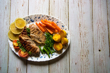 Top view of grilled chicken steak with vegetables on a background