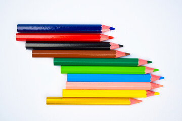 Lot of different colored wood pencil crayons scattered on a white background
