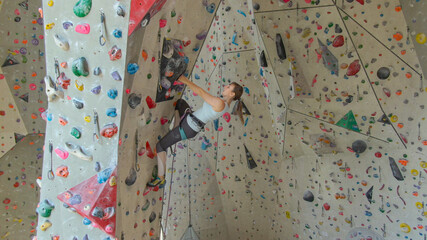AERIAL: Flying near an athletic woman indoor lead climbing up a difficult route.