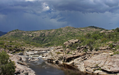 The rapids. View of the pure water river flowing across the stone valley in the mountain forest under a stormy sky. The strong current, rocky shore and bed.