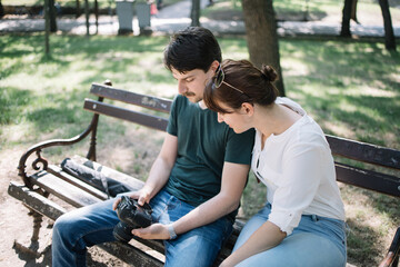 Female model and male photographer checking photos on camera. Man holding camera while sitting on bench next to girl and checking images.