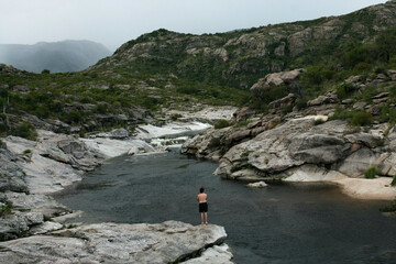 Fototapeta na wymiar The rapids. Adult caucasian man standing in the rocky cliffs contemplating the natural landscape. The river flows along the stone valley in the forest and hills. 
