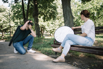 Squatting man with professional camera photo shooting female model. Side view of girl sitting on...
