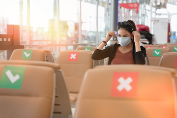 Asian tourist woman wearing a face mask or face shield sitting and waiting for boarding at the airport terminal, social distancing, travel bubble, new normal lifestyle concept, traveling alone.