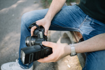 Close-up view of man's hands holding professional camera. Cropped man holding DSLR camera with flash while sitting outdoor.