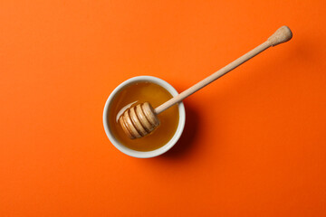 Bowl with honey and dipper on orange background, top view