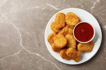 Plate with fried chicken nuggets and ketchup on gray table, top view