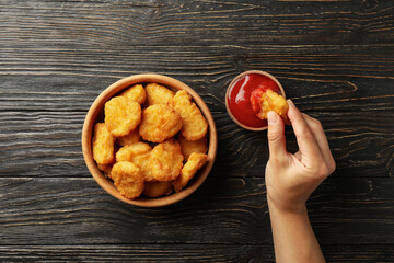 Female hand holds nugget over the wooden background with bowl of nuggets