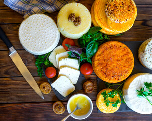 Cheese Heads with cheeses of different kinds. Assortment of different cheese types on wooden background. Fresh dairy product, various greens, nuts, honey, healthy organic food. Delicious apetizer