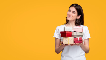 Holiday sale. Special offer. Cheerful woman in white t-shirt holding gift boxes pile isolated on orange copy space. Happy birthday. Festive occasion. Greeting congratulation.