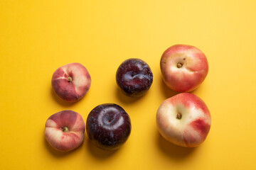 Kernel summer fruits flat lay on yellow. Top view of a combination of pit fruits like chinese flat donut peaches, nectarines and blue plums over a mustard yellow desk. Minimal flat lay style