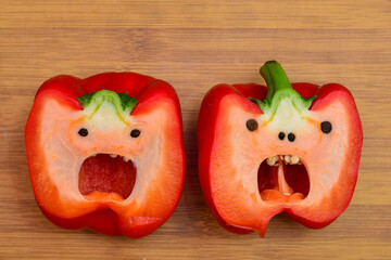 Two large red peppers, cut in half on a cutting board, looks like a face