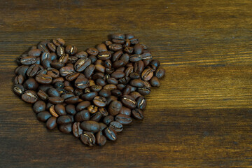 Heart shaped coffee beans on brown wooden background. Top view or macro of heart shaped fresh organic roasted coffee beans on wooden surface. Lovely coffee beans with wooden table.  Place for text