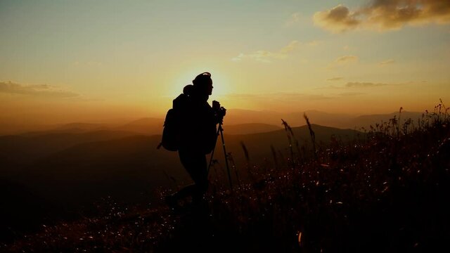 Epic shot of a woman hiking on the edge of the mountain in beautiful sunset. Camera follows hipster millennial young woman running up on top of mountain summit at sunset