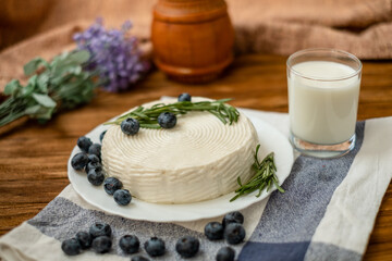 A glass of goat milk and a head of goat milk cheese stand on a wooden table. Cheese at home.