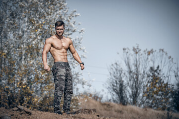 Bodybuilder posing shirtless outdor. Trees background. Perfect body.