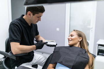 Close up portrait of beautiful young lady sitting in dental chair while stomatologist hands in sterile gloves holding tooth samples.