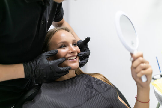 Patient in dental chair. Dentist's hands with gloves ckeck smile of pacient. Beautiful young woman having dental treatment at dentist's office.