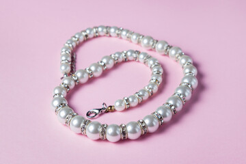 White pearl decoration on a pink background. Women's accessory. Glamorous decoration