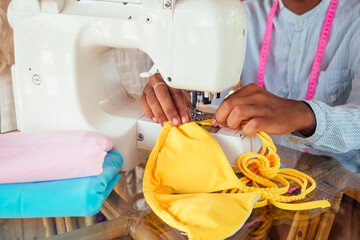 african american woman sewing a stylish yellow swimming suit for summer pool party in tropical workshop in Bali