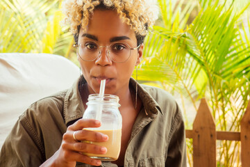 beautiful brazilian smiling girl drinking cold icy coffee or smoothie in cafe from a glass jar