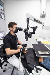 Male dentist examining patient looking on the teeth with professional microscope at surgery dental office