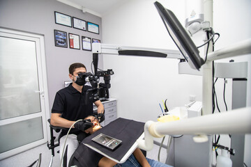 Male dentist examining patient looking on the teeth with professional microscope at surgery dental office