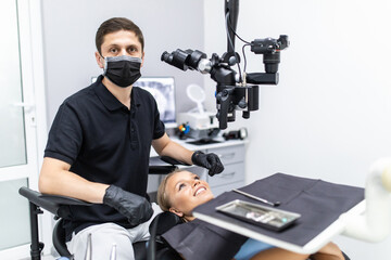 Handsome dentist sitting in chair, posing, looking at camera. Dentist man working in private dentistry clinic with modern equipment, professional microscope.