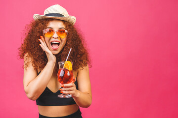 Happy beautiful curly woman in summer casual clothes with a glass of cocktail drink studio shot isolated on colorful pink backgroud.