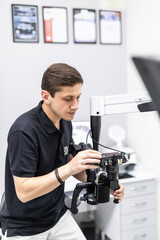 Mature stomatologist posing on workplace, near dental microscope, leaning on dentist chair. Handsome, bearded stomatologist wearing in white medical coat.