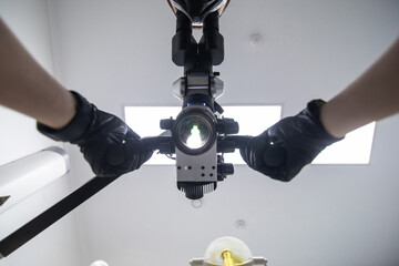 Rational doctor is using the dental microscope in the clinic. The microscope is glowing. View from the bottom. Vertical.