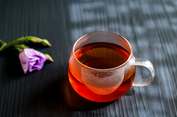black tea in a transparent Cup next to a purple flower on a dark wooden background