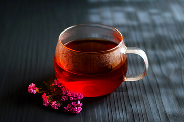 black tea in a transparent Cup next to a purple flower on a dark wooden background