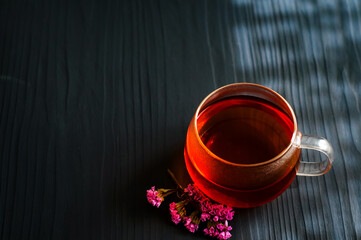black tea in a transparent Cup next to a purple flower on a dark wooden background