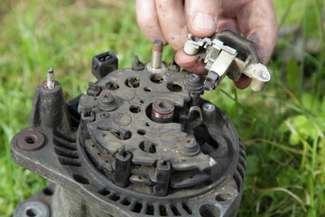 Relay voltage regulator in hands on used car 12 V alternator background close up, outdoor vehicle...